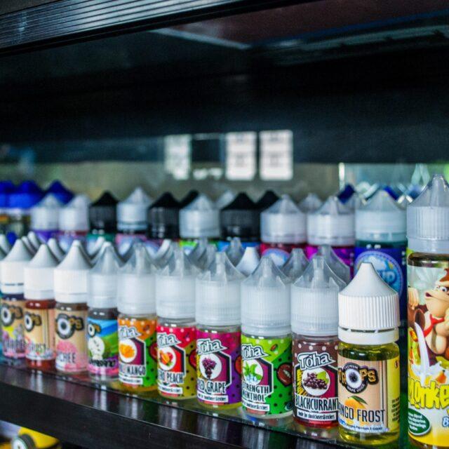 Rows of colorful e-liquid bottles displayed on shelves in a vape shop.