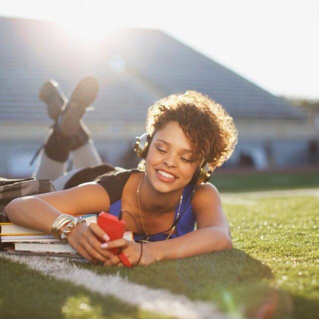 Young woman lying on grass, taking a selfie with a bright smile.