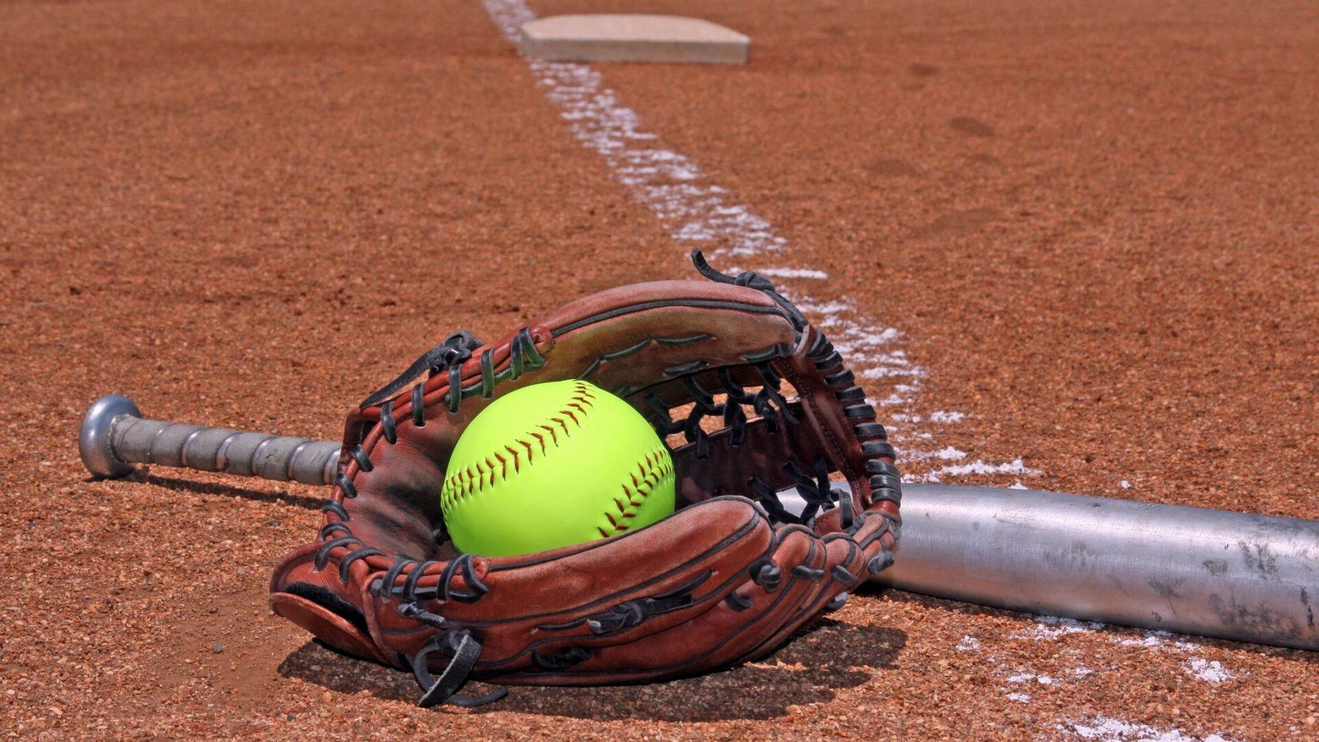 A softball resting inside a glove on a baseball field near home plate.