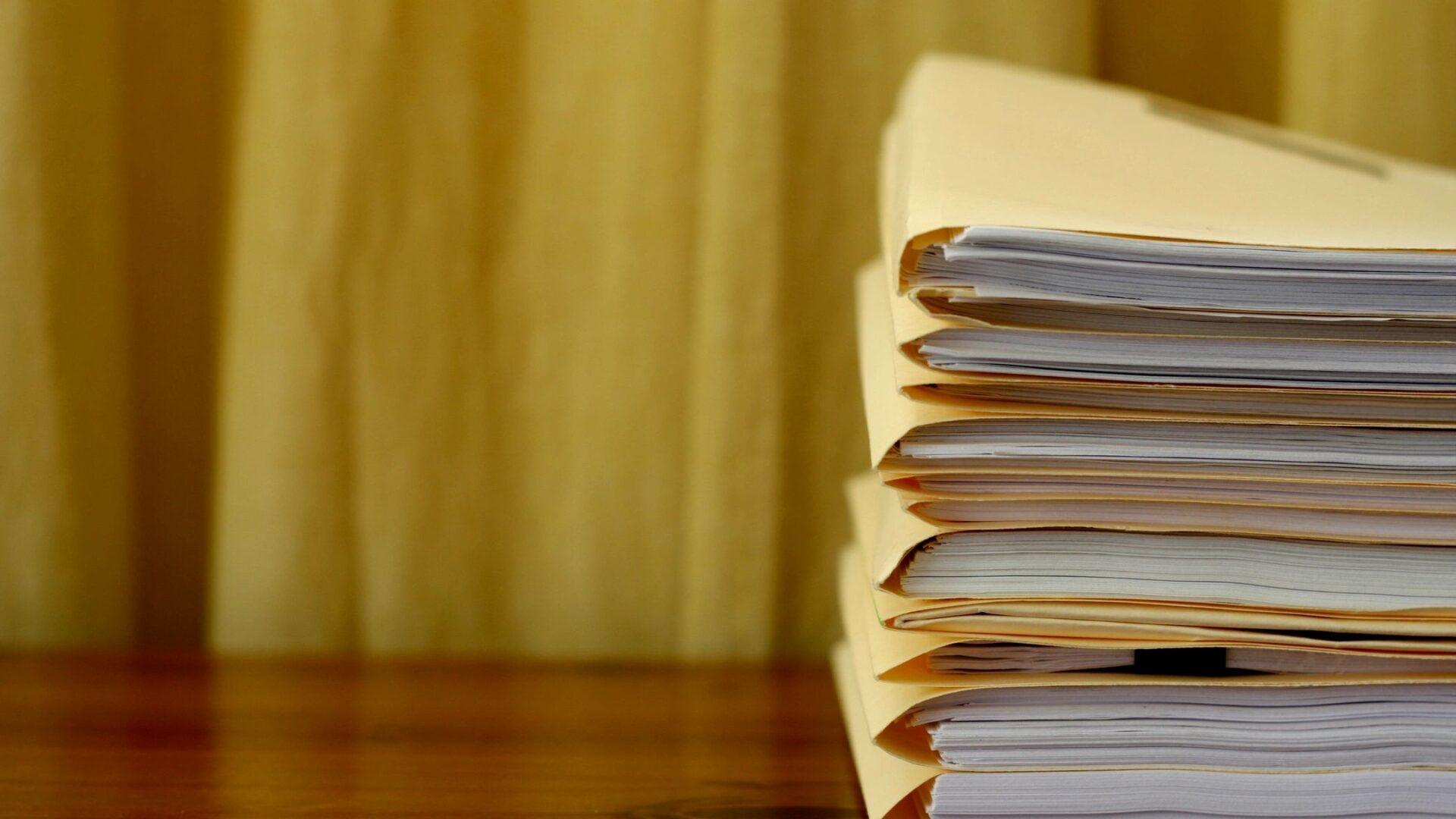 Stack of folded papers on a wooden table with a blurred yellow background.