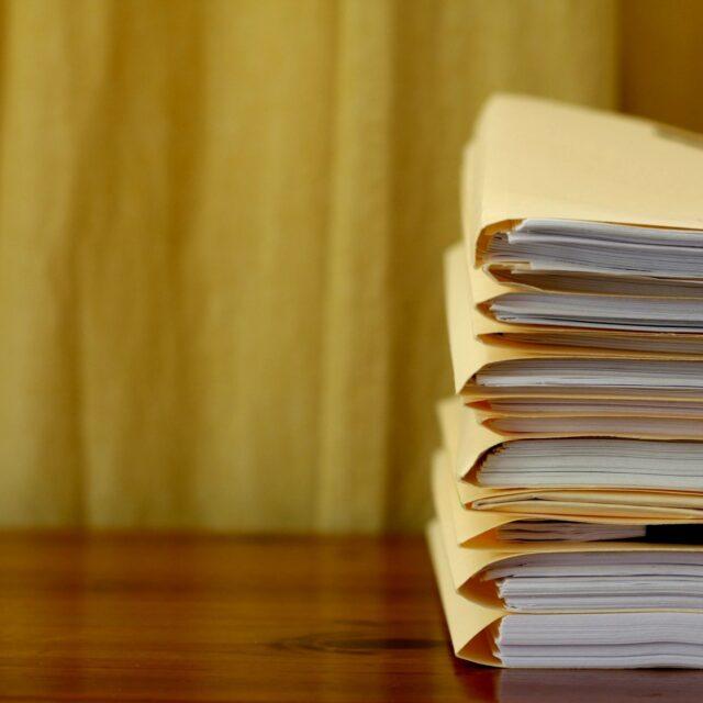 Stack of folded papers on a wooden table with a blurred yellow background.