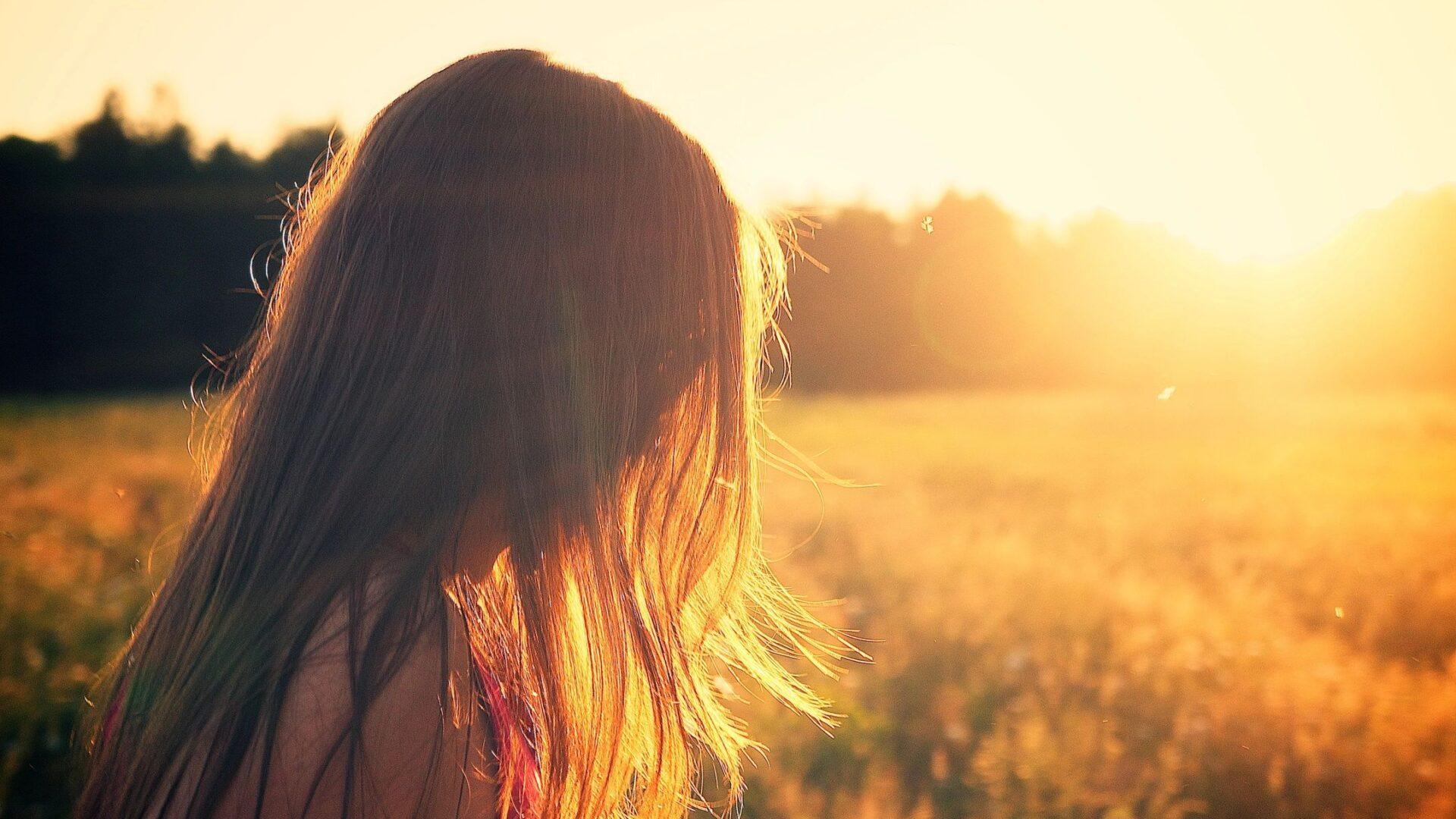 A woman gazes at the sunset over a golden field.