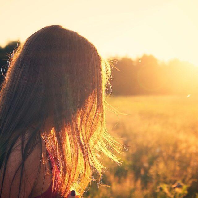 A woman gazes at the sunset over a golden field.