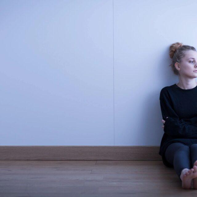 Woman sitting alone against a wall, looking contemplative.