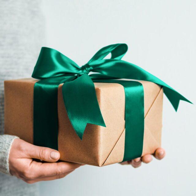 A hand holding a gift wrapped in brown paper with a green ribbon.